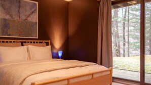 Ein Schlafzimmer mit einem großen Bett, einem Nachttisch, einer Lampe und einem Fenster mit Blick auf Bäume.