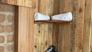 Un coin de pièce avec des lambris en bois, deux serviettes posées sur une étagère, un sèche-cheveux et un petit récipient.