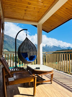 A wooden deck with a hanging chair and a table, overlooking a mountainous landscape. - Hostelam The Mountain Story (Manali)
