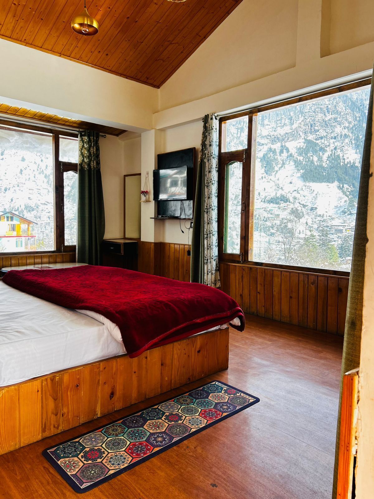 A bedroom with a wooden bed, a TV, and large windows with a view of a snowy landscape.