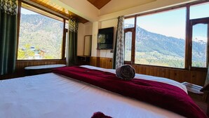 A bedroom with a large bed, a television, and a view of a mountainous landscape. - Hostelam The Mountain Story (Manali)