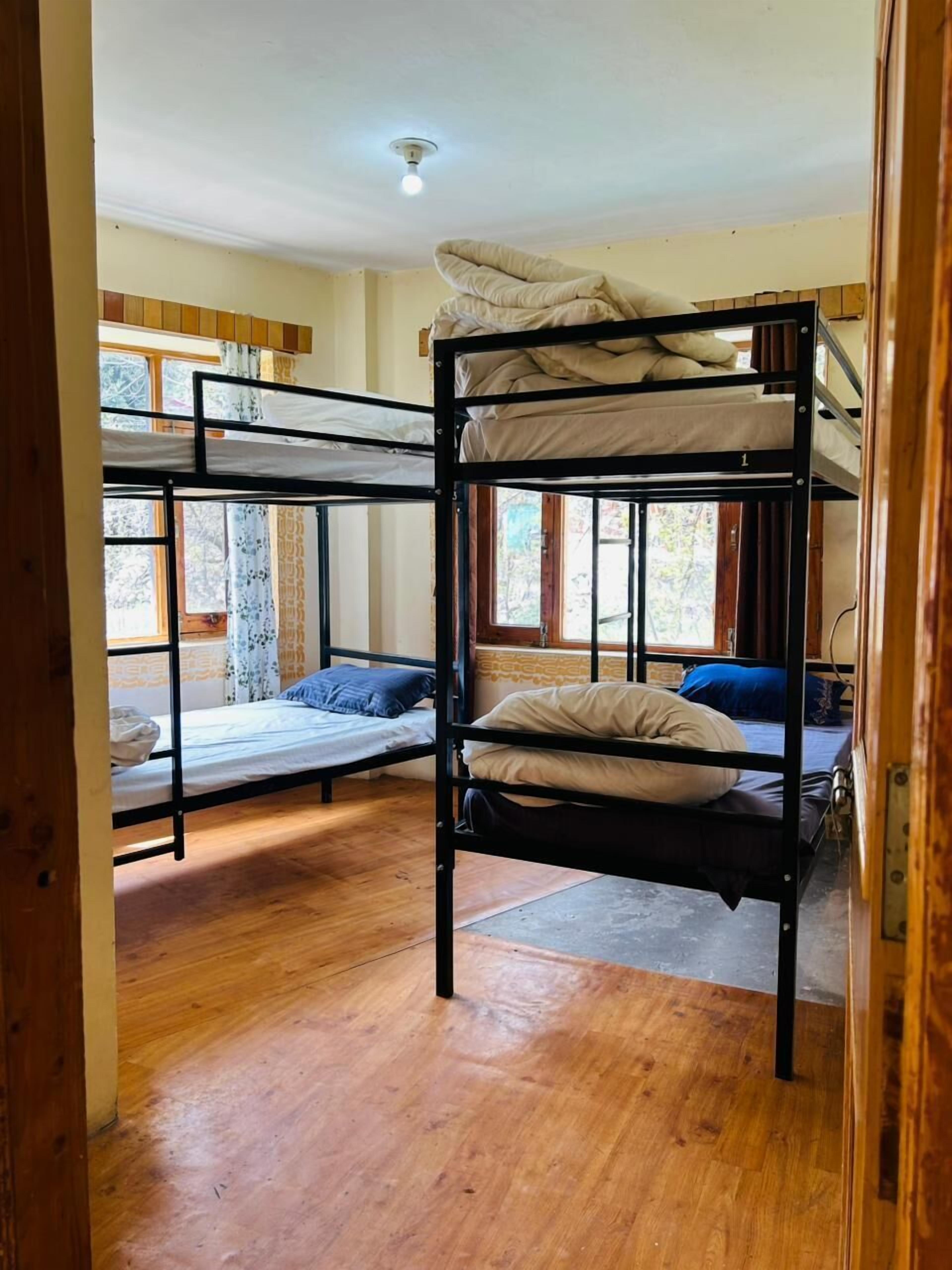 Habitación con literas, suelo de madera, ventana con cortinas y una lámpara en el techo.