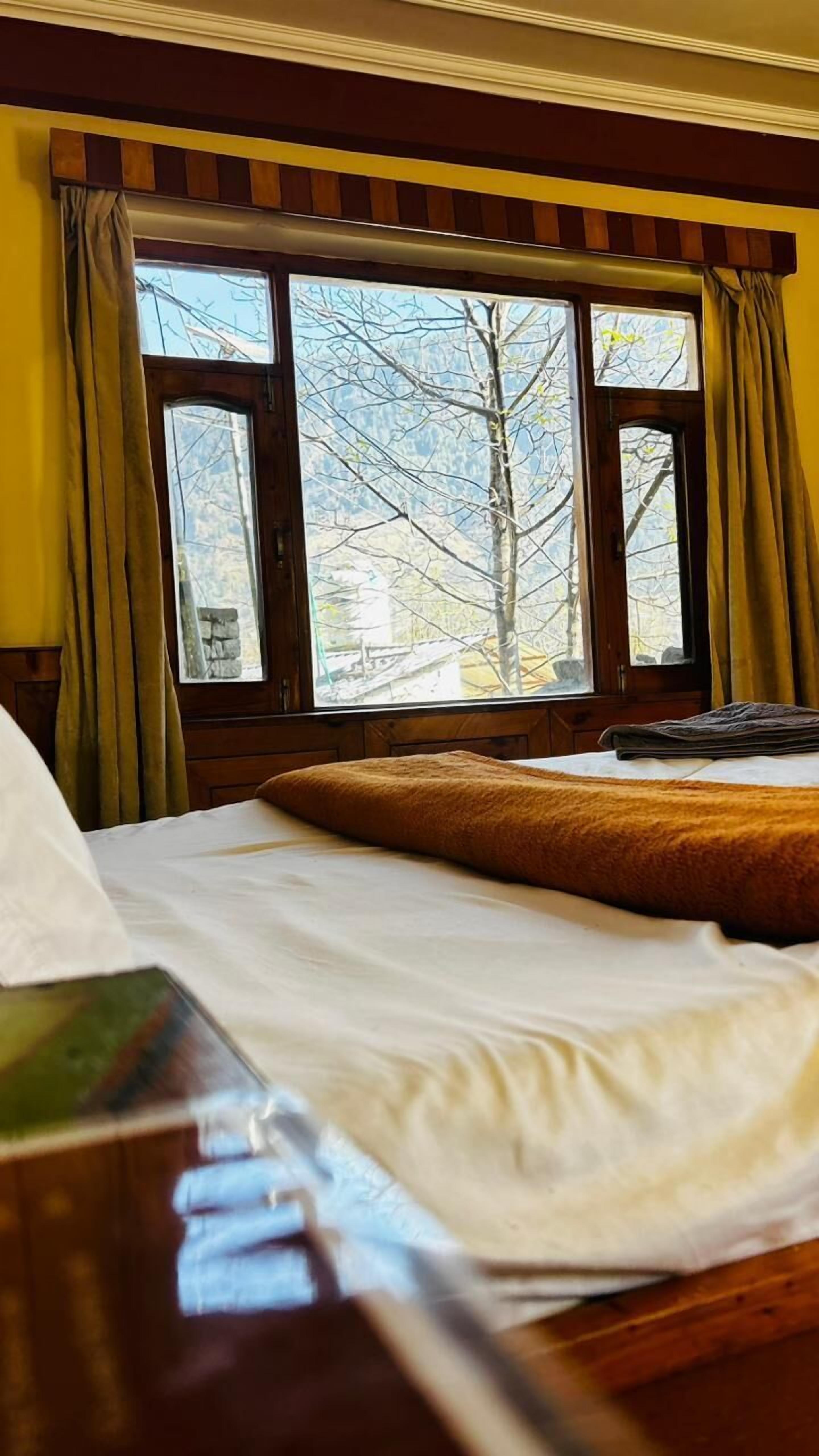 Une chambre d’hôtel avec un lit, une fenêtre avec des rideaux et une vue sur les arbres à l’extérieur.