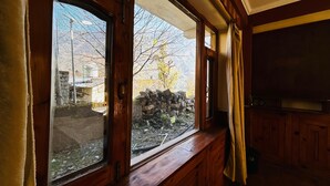 A room with wooden walls, a stone wall outside, and a window with a view of a tree and a building. - Hostelam The Mountain Story (Manali)