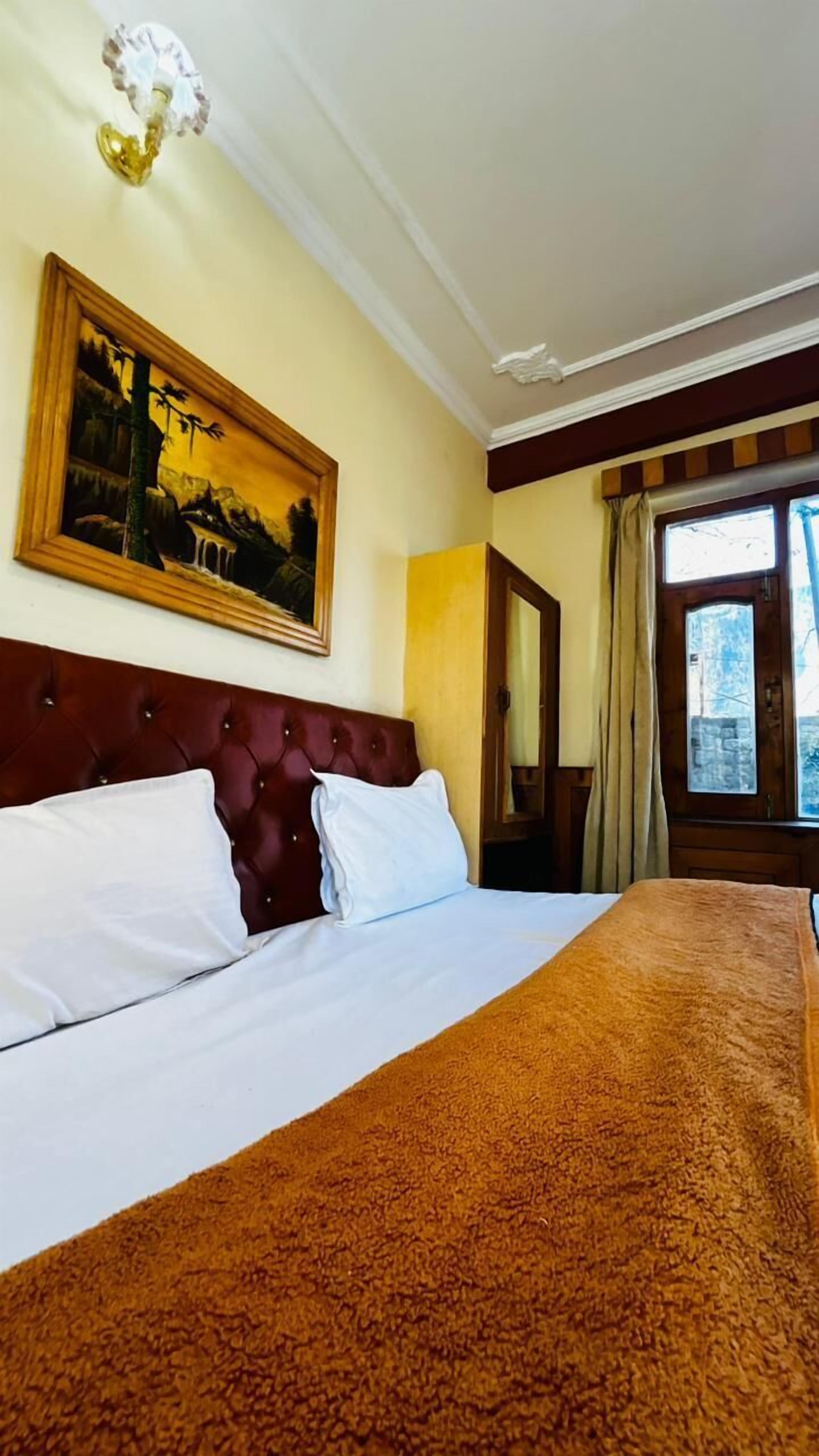 Een hotelkamer met een groot bed, een schilderij aan de muur, een raam met gordijnen en een houten hoofdeinde.