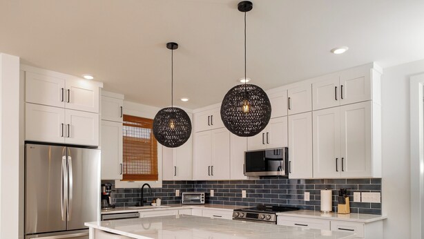 Una cocina moderna con armarios blancos, electrodomésticos de acero inoxidable, una isla central con taburetes de bar e iluminación colgante.