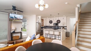 Una cocina moderna con armarios blancos, una isla central y un comedor con una mesa redonda y sillas.