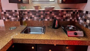 A compact kitchen with dark wooden cabinets, a tiled backsplash, a stainless steel sink, and a portable gas stove. - Feel like home one bedroom studio 
full kitchen, Near Satisima Trinidad Church (Malolos)