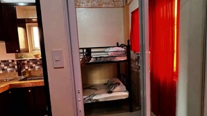 A compact room with a bunk bed, a kitchenette, and a sliding door with red curtains. - Feel like home one bedroom studio 
full kitchen, Near Satisima Trinidad Church (Malolos)