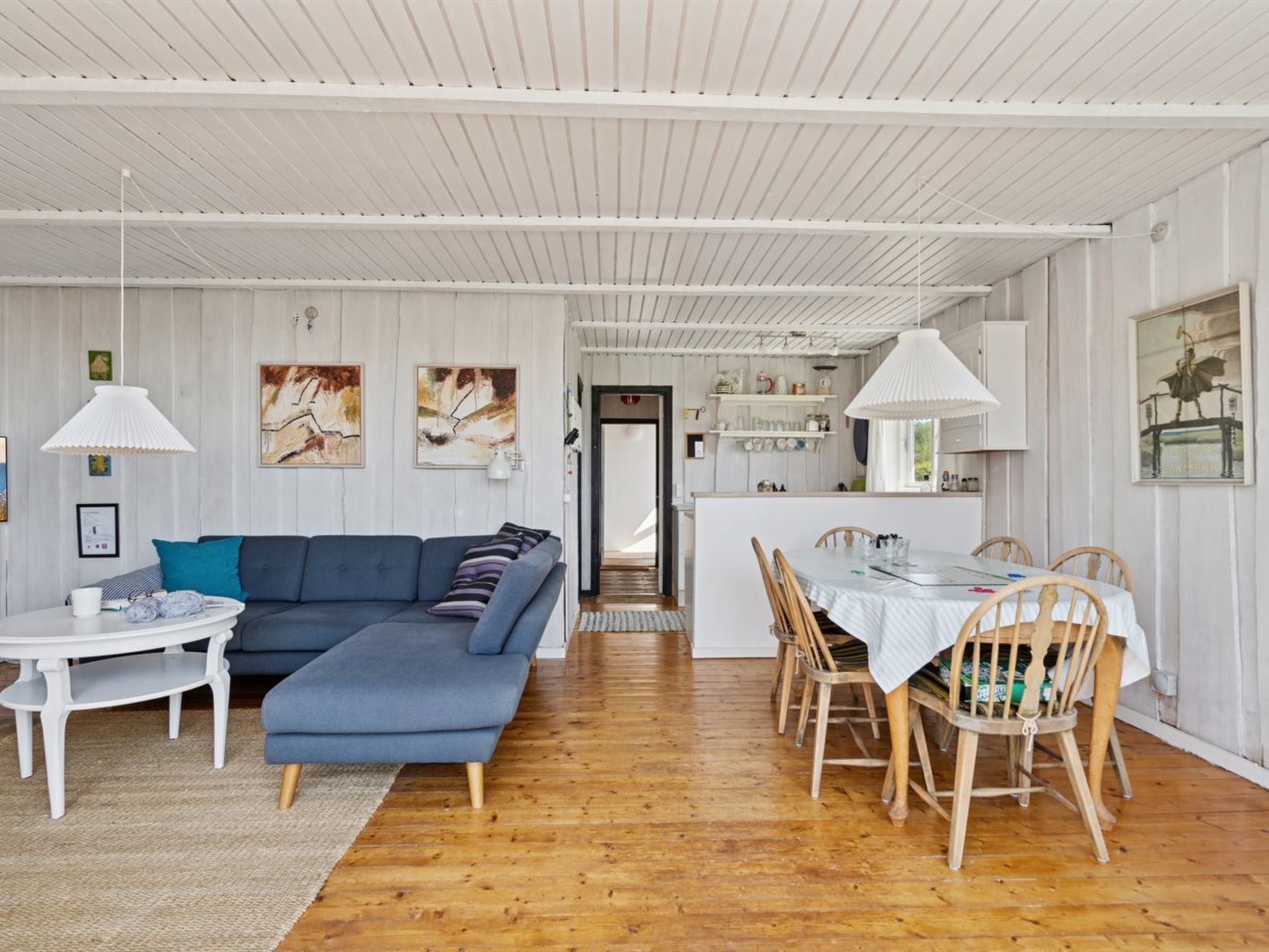 Ein modernes Wohnzimmer mit einem blauen Sofa, einem weißen Esstisch und Holzstühlen.