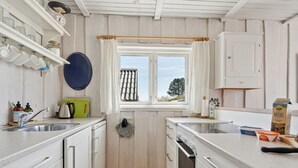 A compact kitchen with white cabinets, a window with curtains, a hanging pot rack, and a wooden floor. - "Hira" - 200m from the sea by Interhome (Egernsund)