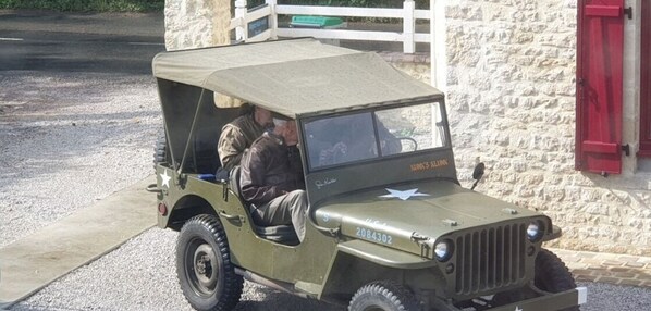 A vintage military jeep parked in front of a stone building with a red door. - Cocooning gîte close to the D-Day landing beaches, ideal for historical visits (Englesqueville-la-Percée)