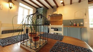 Een eetgedeelte met een houten tafel, een plant in een metalen kooi, en een keuken op de achtergrond.