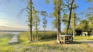 Une jetée en bois menant à une étendue d’eau, entourée d’arbres et de zones herbeuses.