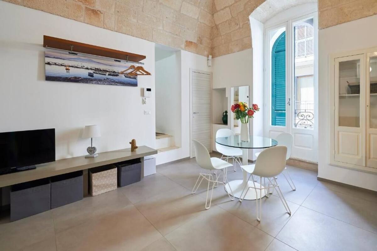 Una cocina moderna con una mesa de comedor de vidrio, sillas blancas, un televisor y una pared de piedra.