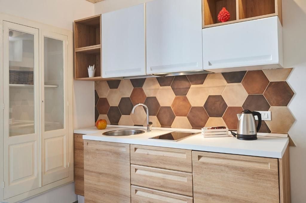 Una cocina con encimera blanca, pileta de acero inoxidable, armarios de madera y un salpicadero de baldosas hexagonales.