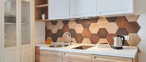 Una cocina con encimera blanca, pileta de acero inoxidable, armarios de madera y un salpicadero de baldosas hexagonales.