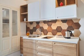 Une cuisine dotée d’un plan de travail blanc, d’un évier en acier inoxydable, de meubles en bois et d’un dosseret en carreaux hexagonaux.