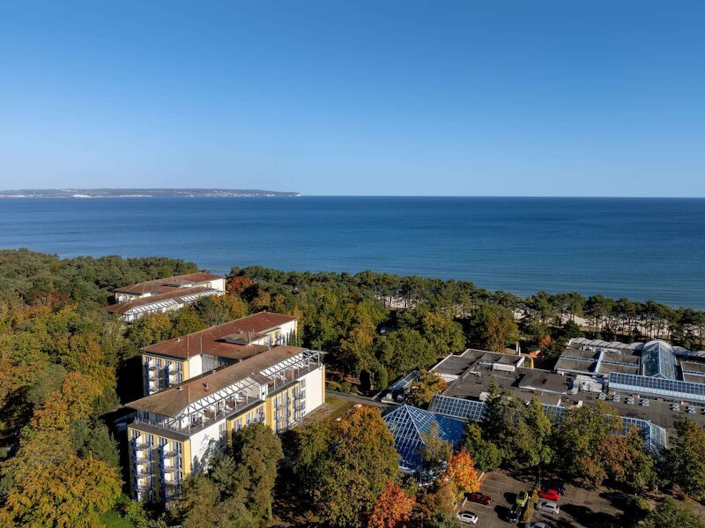 Un hotel costero con varias construcciones, incluyendo una estructura grande con fachada de vidrio y un edificio más pequeño con techo inclinado.