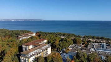 Un hotel costero con varias construcciones, incluyendo una estructura grande con fachada de vidrio y un edificio más pequeño con techo inclinado.