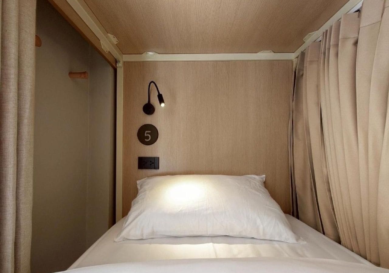 A single bed with a headboard, a wall-mounted light fixture, and a number plate indicating room number 5.