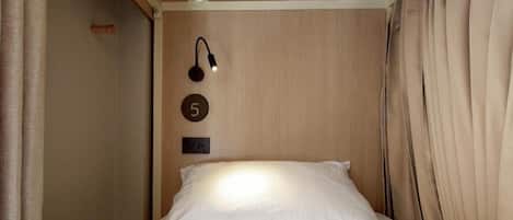 A single bed with a headboard, a wall-mounted light fixture, and a number plate indicating room number 5.