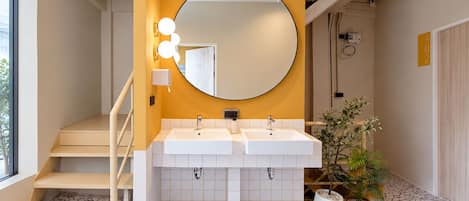 A bathroom with a double sink, a large mirror, and a staircase leading to an upper level.