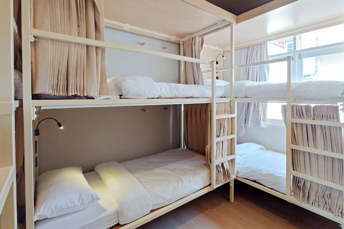 Een slaapkamer met een stapelbed, raam, gordijnen en een bedlampje.