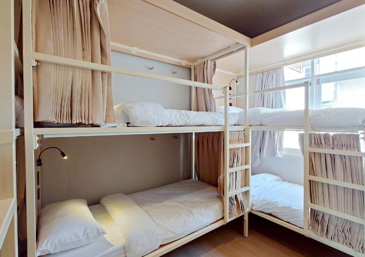 A bunk bed room with a window, curtains, and a bedside lamp.
