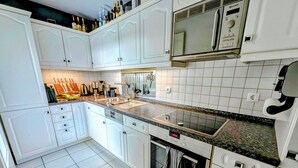 A modern kitchen with white cabinetry, a stainless steel microwave, and a built-in oven. - Vacation apartment with a view of Lake Constance under palm trees (Daisendorf)