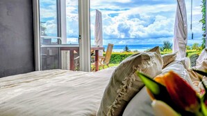 A bedroom with a large bed, a view of the sea, and a sliding glass door leading to an outdoor area. - Vacation apartment with a view of Lake Constance under palm trees (Daisendorf)