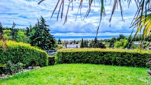 A well-maintained garden with neatly trimmed hedges, a grassy area, and a view of a residential area with houses and trees in the background. - Vacation apartment with a view of Lake Constance under palm trees (Daisendorf)