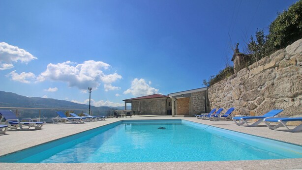 A swimming pool with blue lounge chairs and a stone wall. - Bela Vista Villa with pool for 12 persons (Gerês)