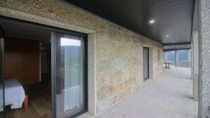 A modern room with stone walls, a wooden floor, and a large sliding glass door leading to a balcony with a view. - Bela Vista Villa with pool for 12 persons (Gerês)