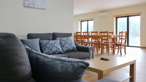 A modern living room with a grey sofa, patterned cushions, a wooden coffee table, and a dining area with wooden chairs and a table. - Bela Vista Villa with pool for 12 persons (Gerês)