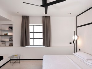 Une chambre à coucher moderne avec un lit, une petite table, une fenêtre avec des rideaux et une étagère remplie de livres.