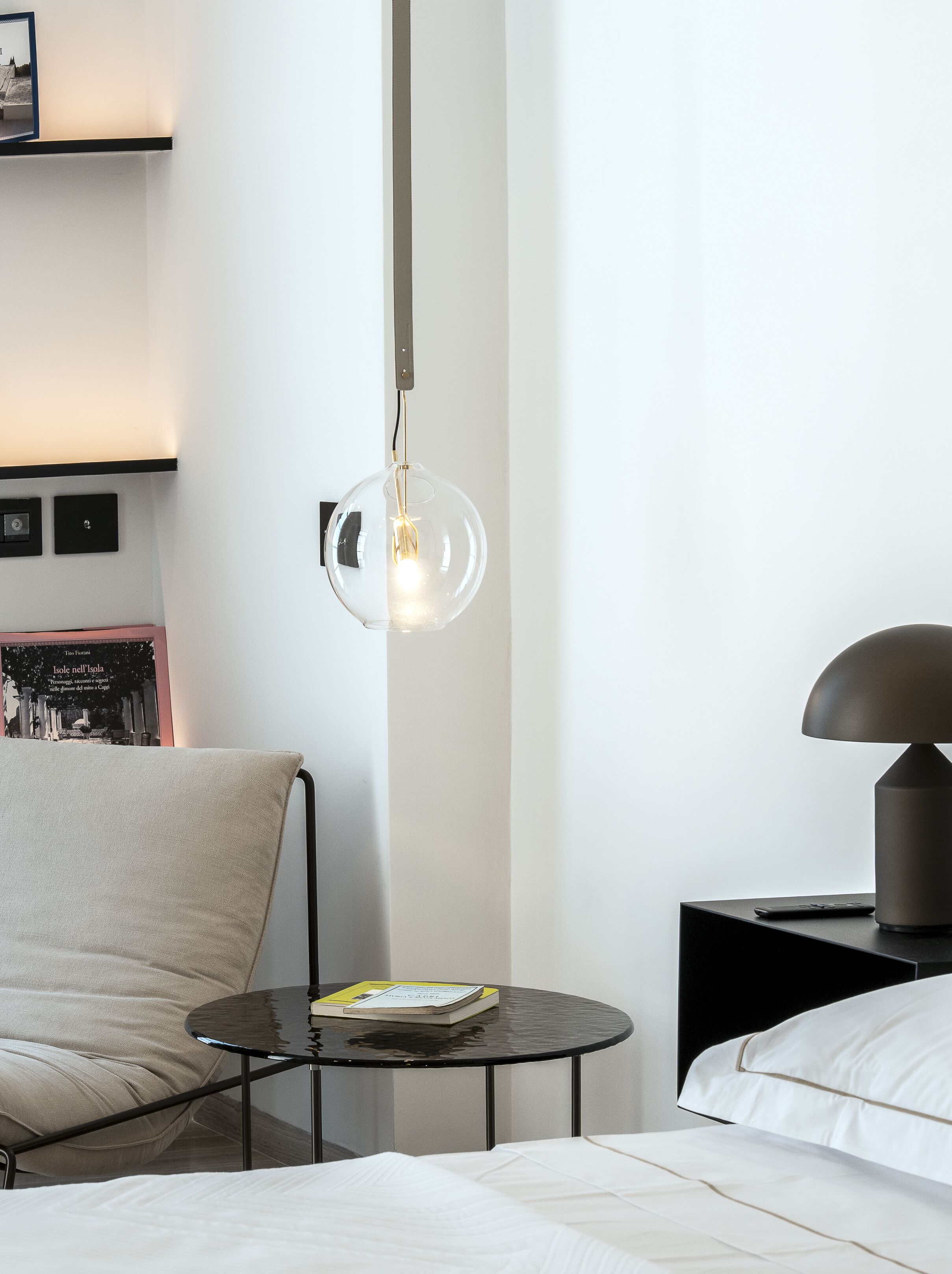 Habitació d'hotel moderna amb una taula rodona, un llit, una làmpada i un llum penjant.