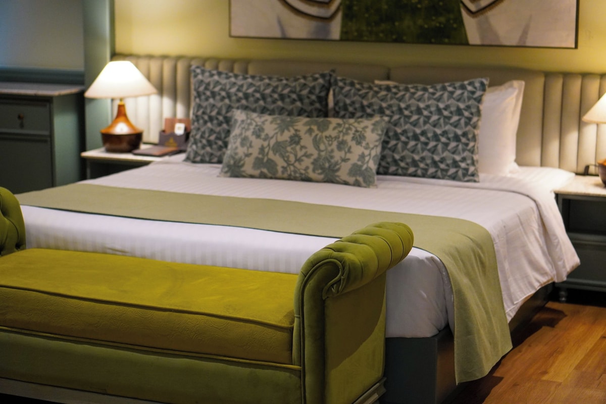 A neatly made bed with a green upholstered headboard, a white bedspread, and multiple pillows with a floral pattern.