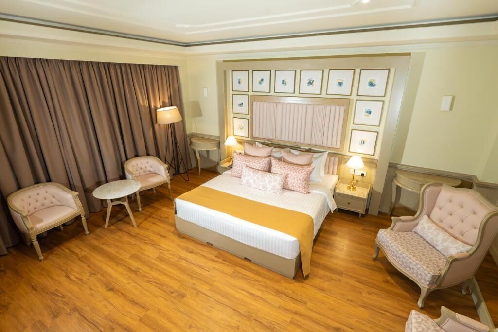 A hotel room with a large bed, two armchairs, a small table, and a nightstand with lamps.