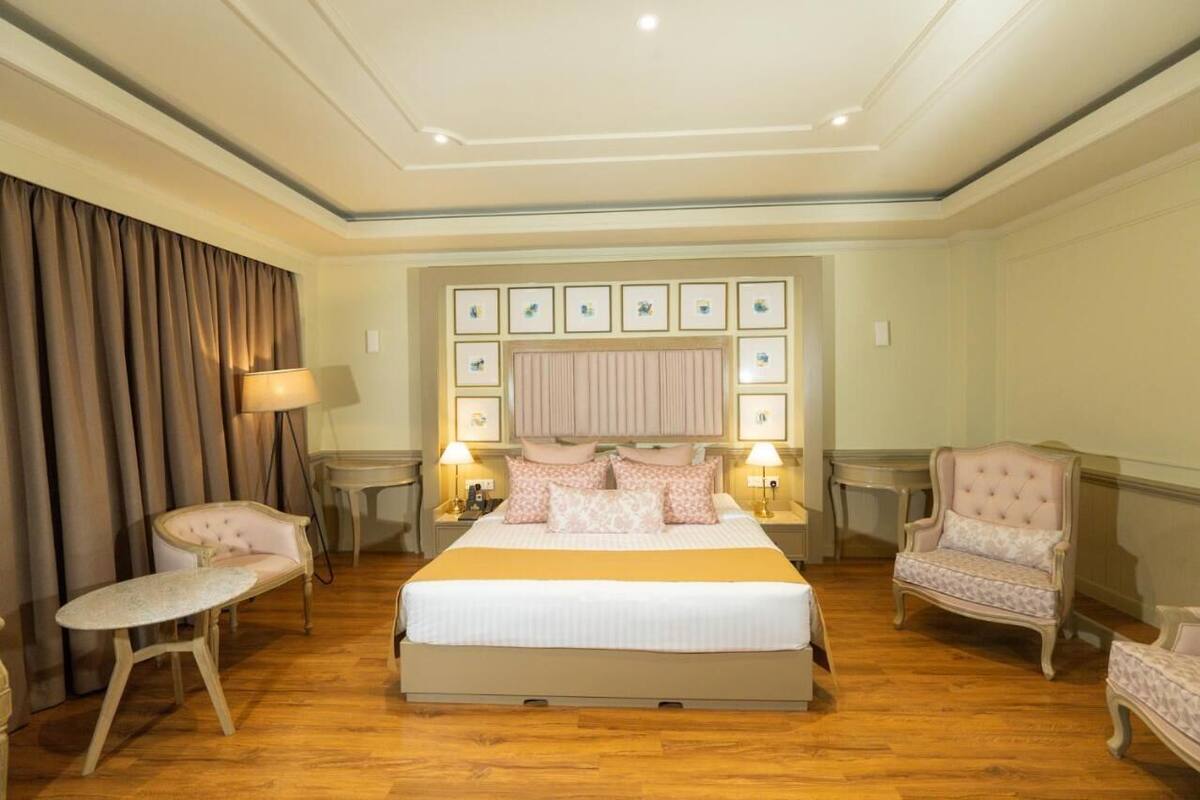 Quarto com uma cama grande, duas mesas de cabeceira com luminárias, cabeceira com quadros emoldurados e duas poltronas estofadas.
