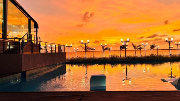 A swimming pool with a sunset view, a covered area with stairs, and street lamps along the water's edge.
