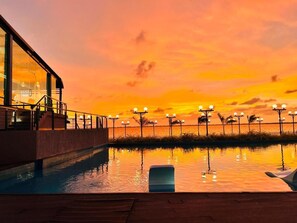 A swimming pool with a sunset view, a covered area with stairs, and street lamps along the water's edge. - Grandeeza Hotel by Galison (Negombo)