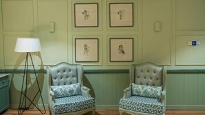 A room with two upholstered chairs with floral upholstery, a floor lamp, and four framed artworks on the wall.