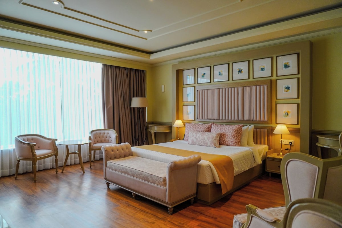 A hotel room with a large bed, two armchairs, a small table, and a bedside table with lamps.