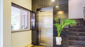A modern elevator with a digital display, a potted plant, and a staircase with dark tiles. - Hotel Johar Inn (Raipur)