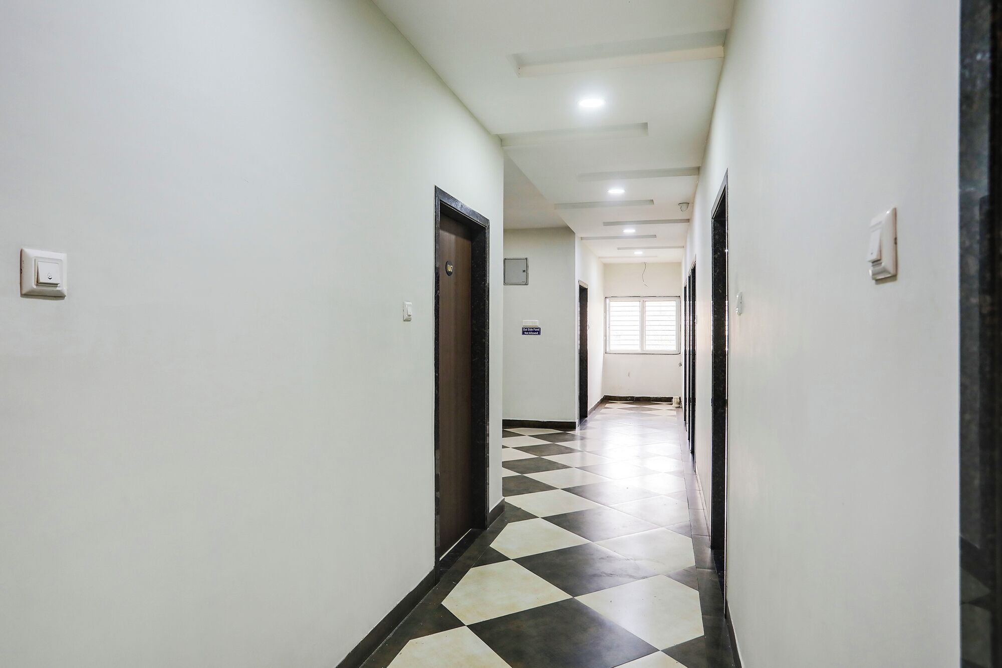 A corridor with a checkered floor, white walls, and doors on both sides.