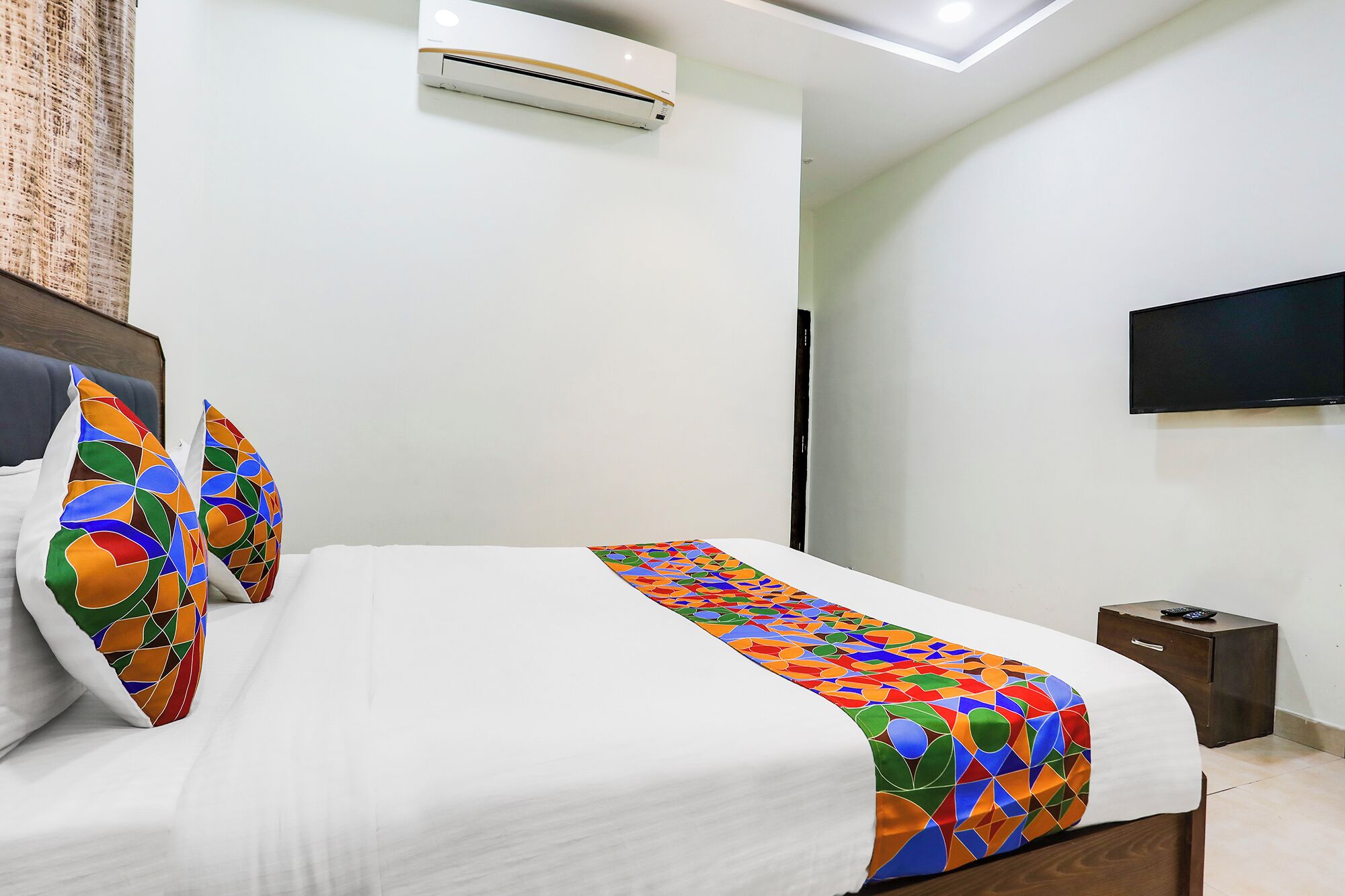Una cama bien hecha con una colcha de estampado geométrico y colores vivos, un almohón blanco y otro a juego a la izquierda.