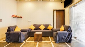 A living room with a sofa set, a coffee table, and a television mounted on the wall. - Hotel Johar Inn (Raipur)