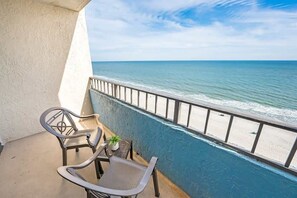 A balcony with a view of the ocean, featuring two chairs and a small table with a plant.
