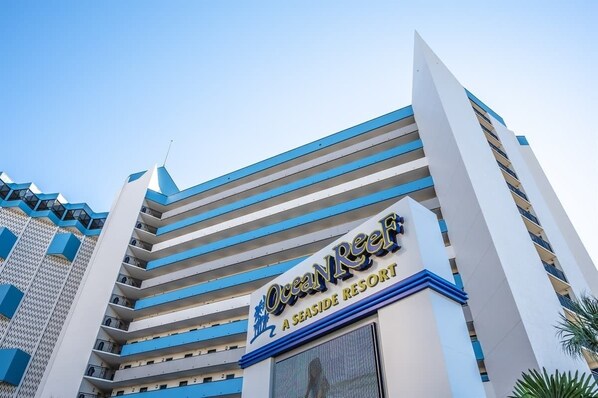 The Ocean Reef A Seaside Resort building facade with a modern design, featuring multiple balconies and a clear sky.